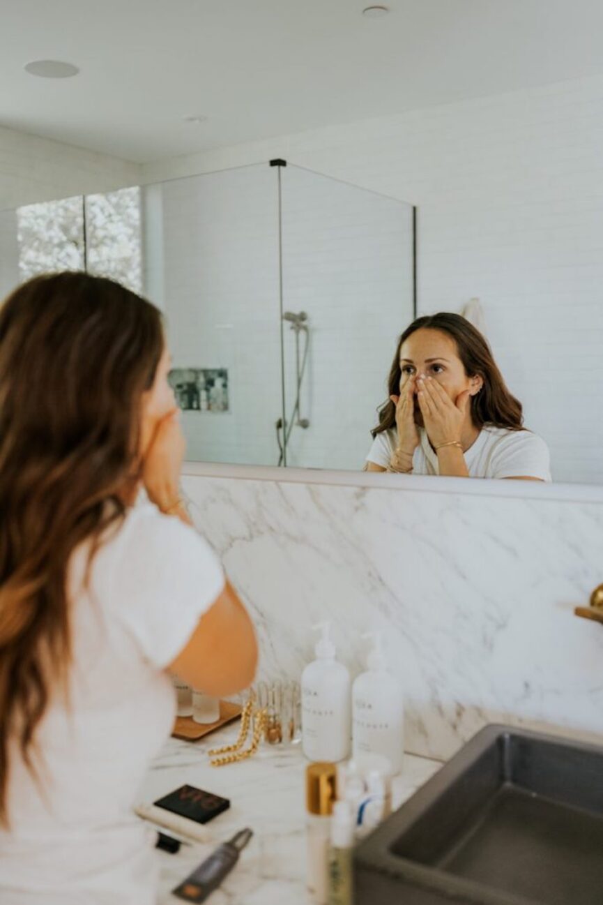 Woman applying skincare in mirror.