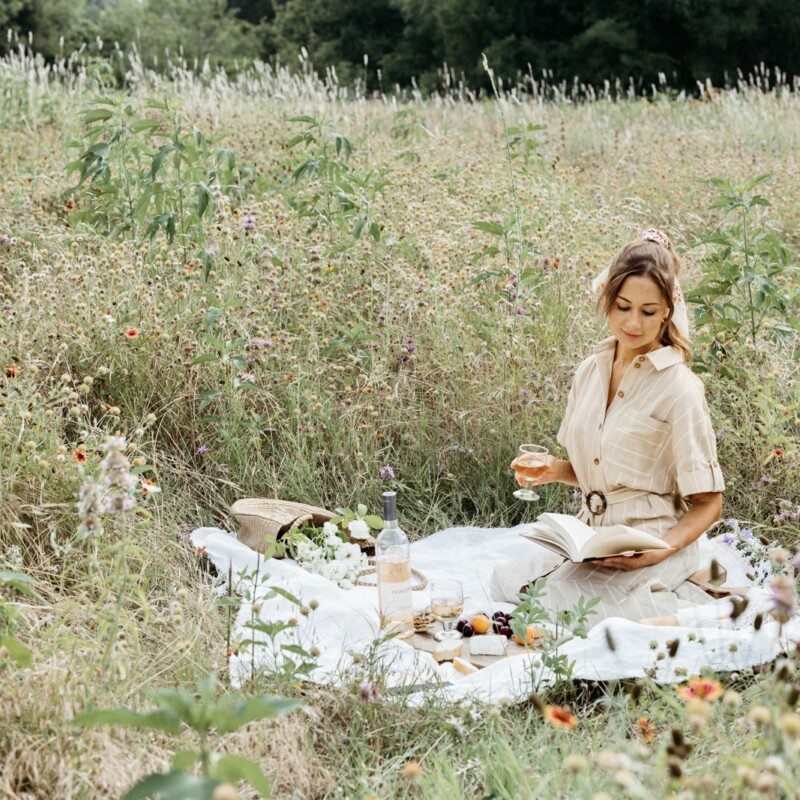 french inspired aesthetic picnic with a woman sitting in a field of wildflowers