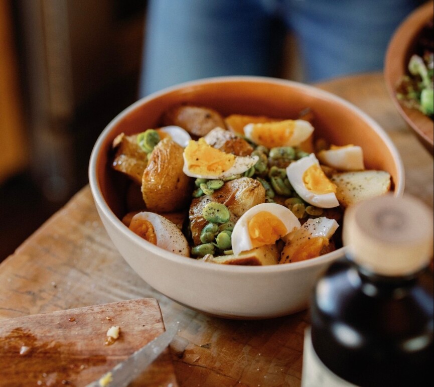 Off-white bowl of simple potato salad recipe with soft-boiled eggs.