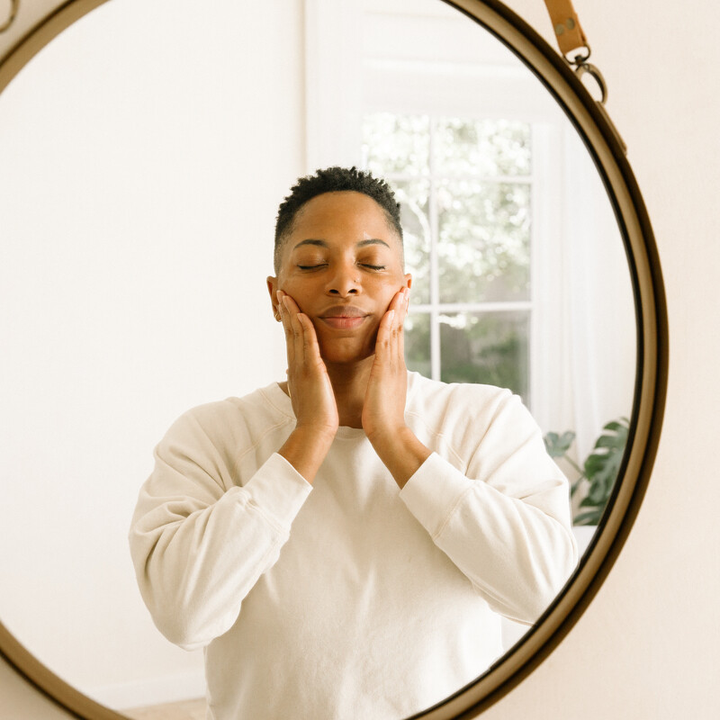 Woman applying skincare products in mirror.